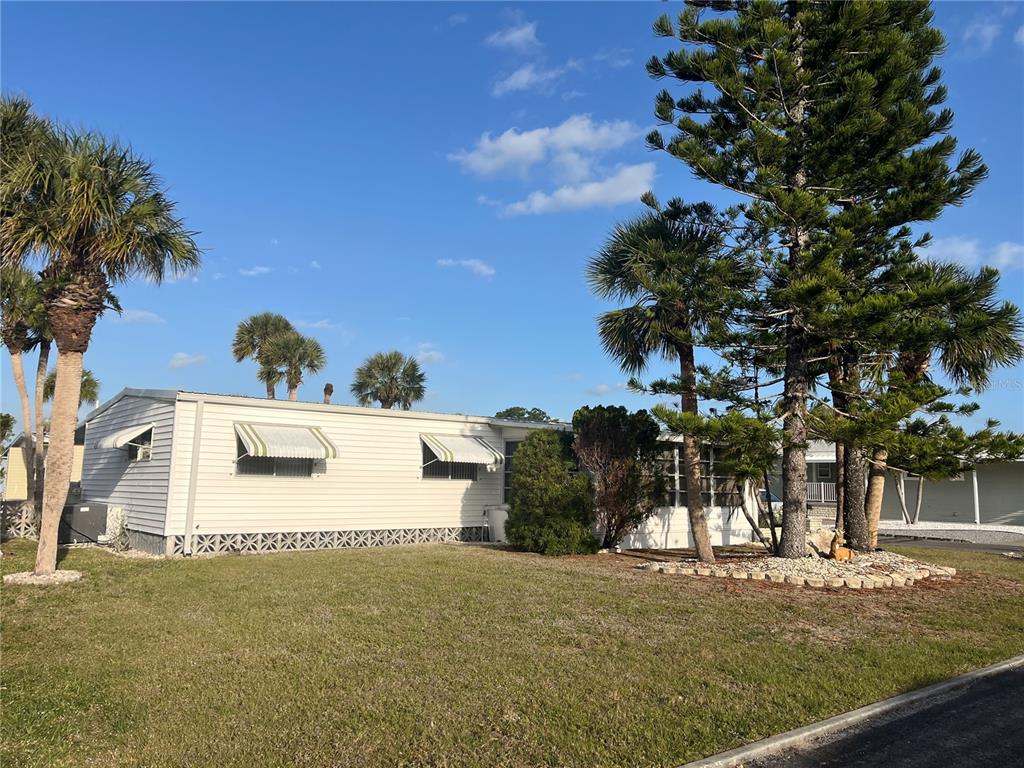 A single-story mobile home with white siding and striped window awnings sits on a grassy lot — 532 VIA VENETO, VENICE, FL