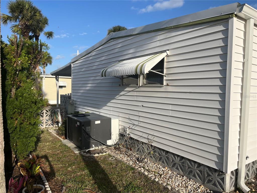 The exterior side of a light-colored mobile home features an air conditioning unit and window awning — 532 VIA VENETO, VENICE, FL