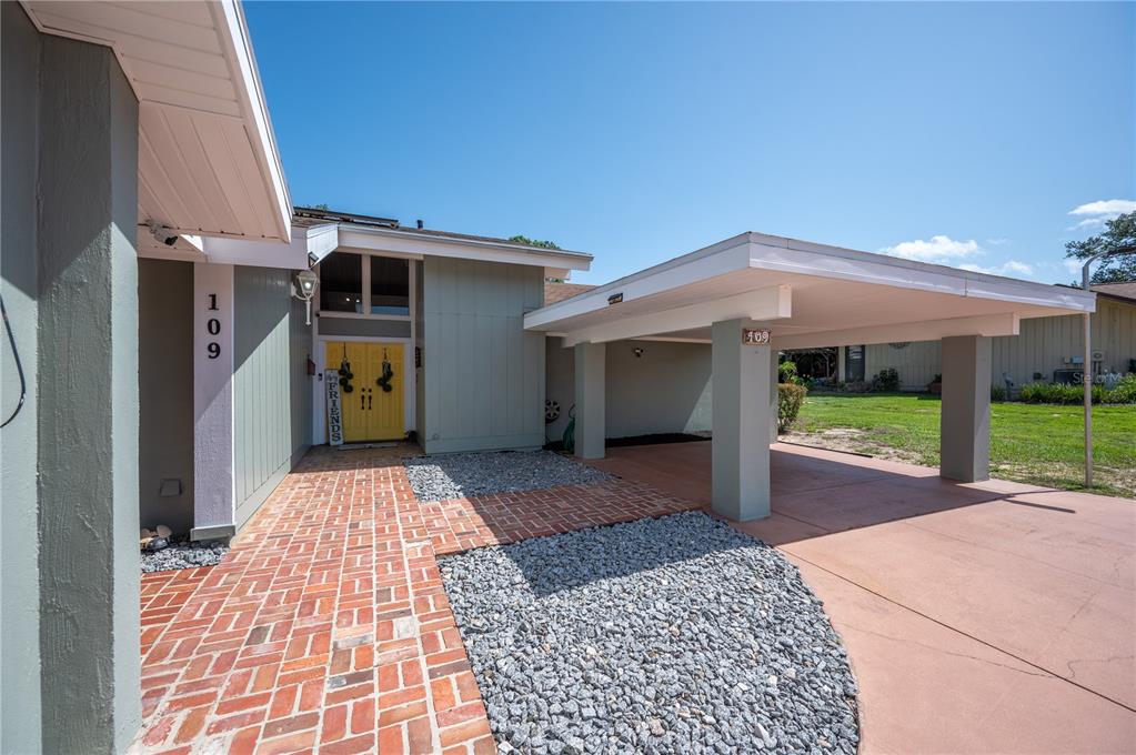 A house exterior features a brick walkway, a yellow front door, and a covered carport — 109 ARROWHEAD LANE, HAINES CITY, FL