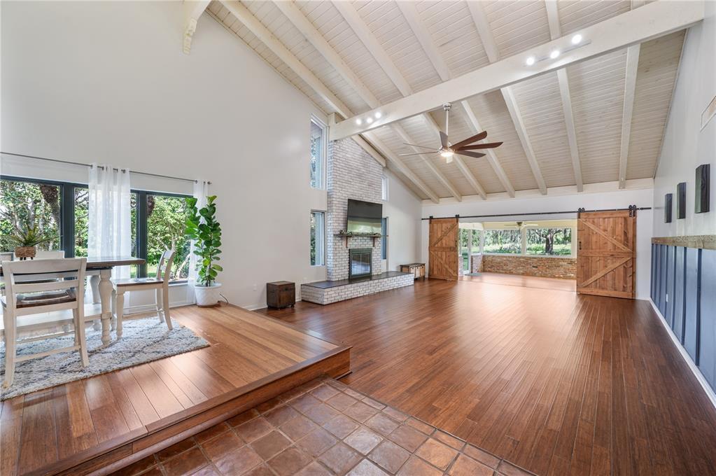 A spacious living room features a vaulted ceiling, hardwood floors, a brick fireplace, and barn doors — 109 ARROWHEAD LANE, HAINES CITY, FL