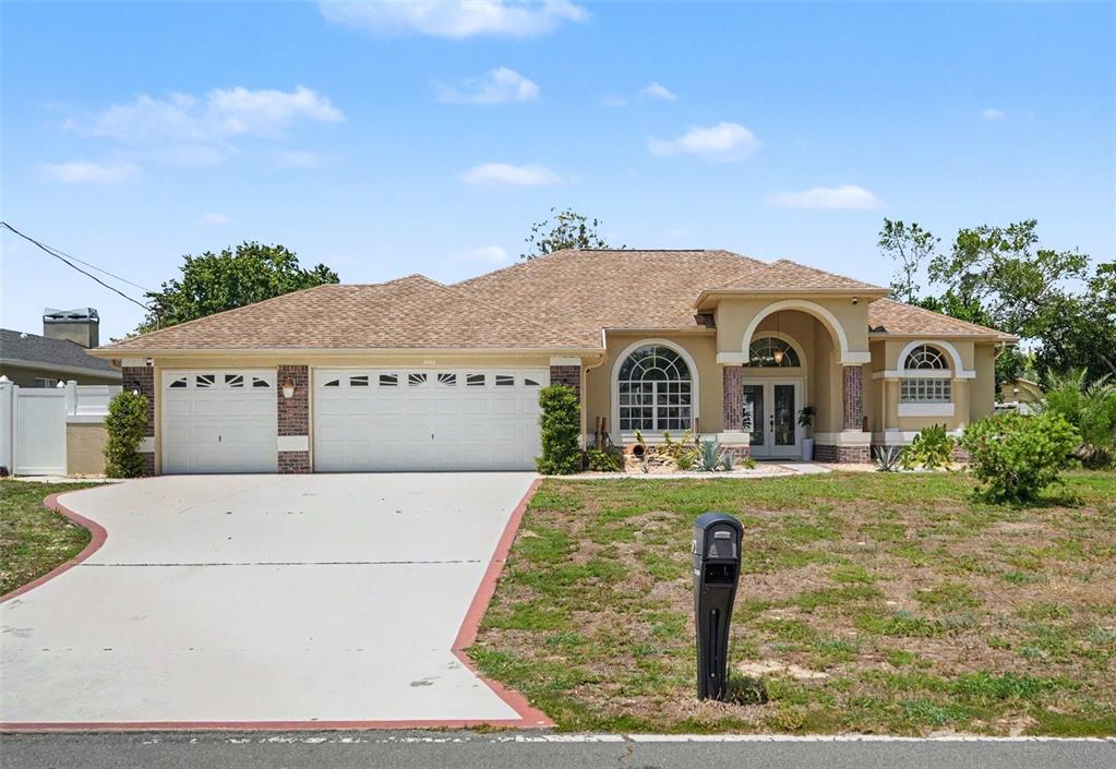 A single-story house with a tan stucco exterior, a three-car garage, and a arched entryway — 3944 LEMA DRIVE, SPRING HILL, FL