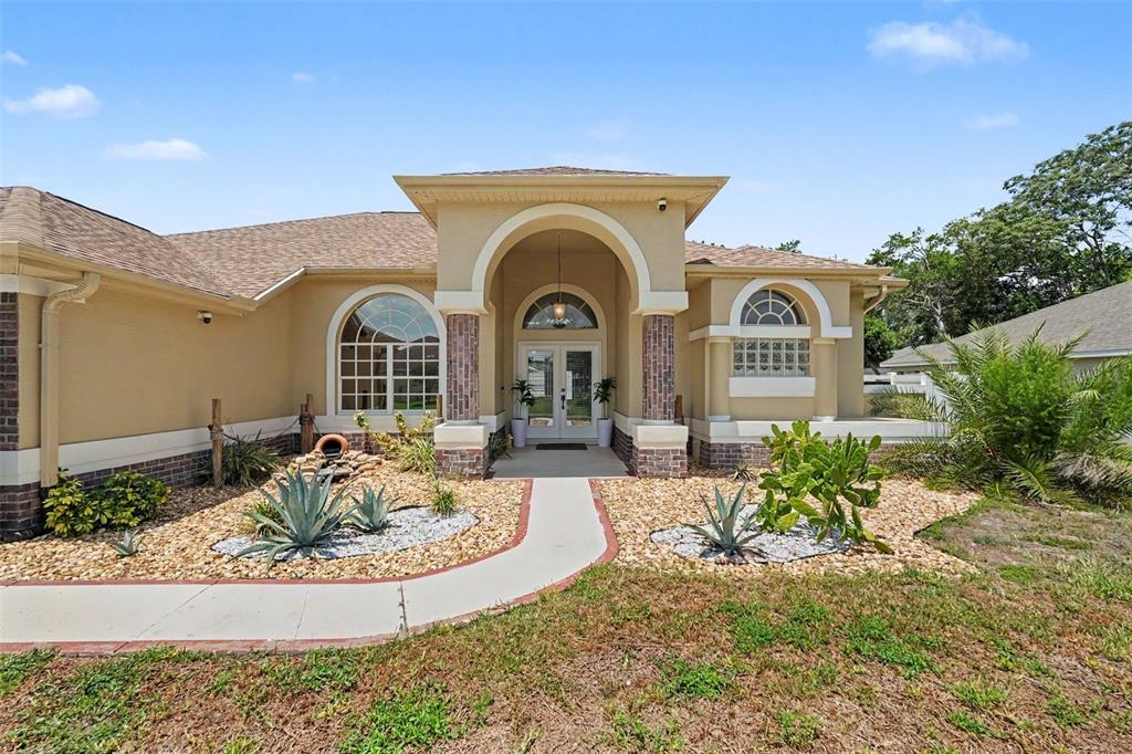 The exterior of a single-story house features a tan stucco facade, arched windows, and landscaping — 3944 LEMA DRIVE, SPRING HILL, FL