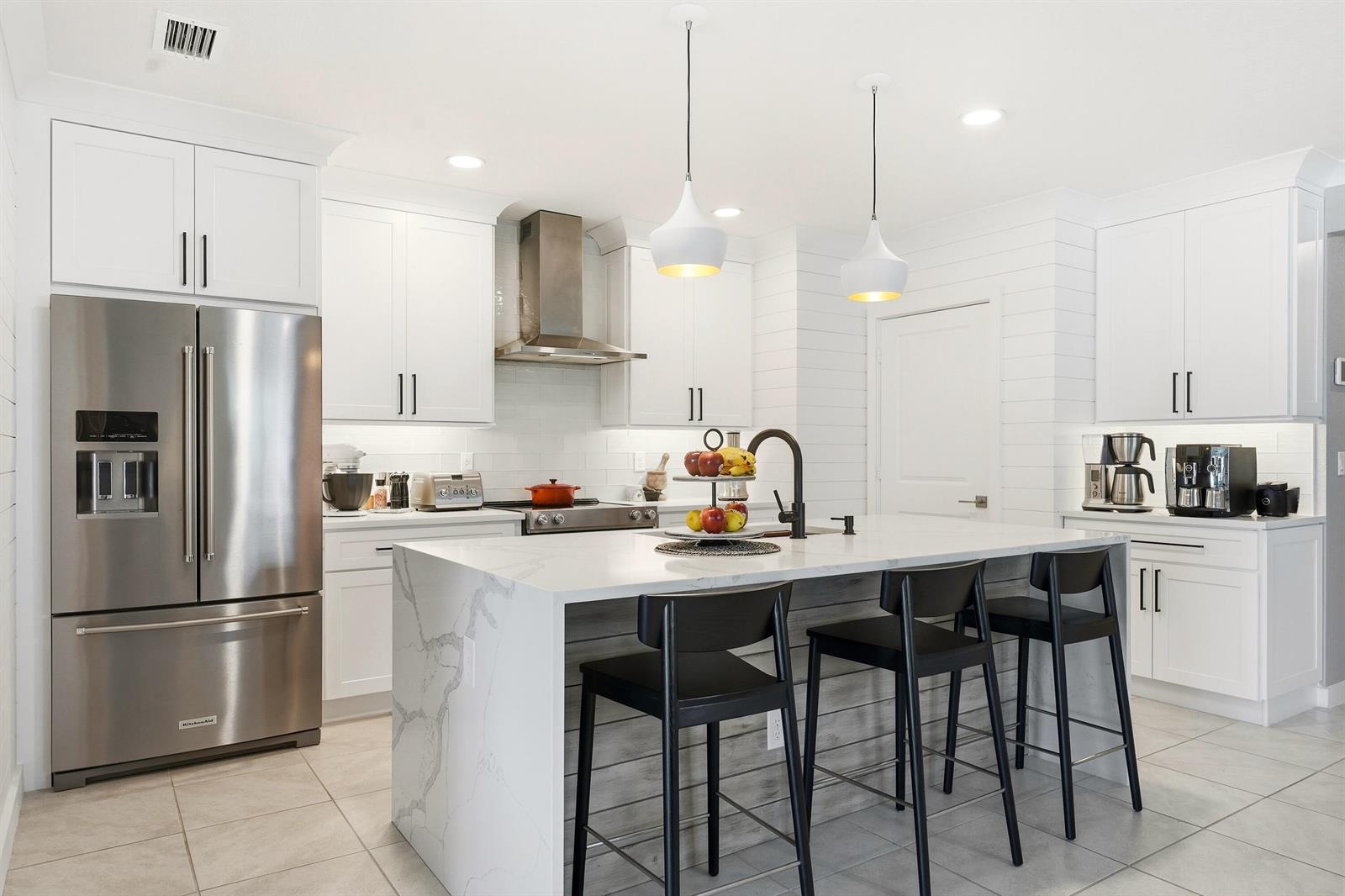 A modern kitchen features white cabinetry, a marble waterfall island, and black bar stools — 3899 SE Lee Street, Stuart FL 34997, STUART, FL
