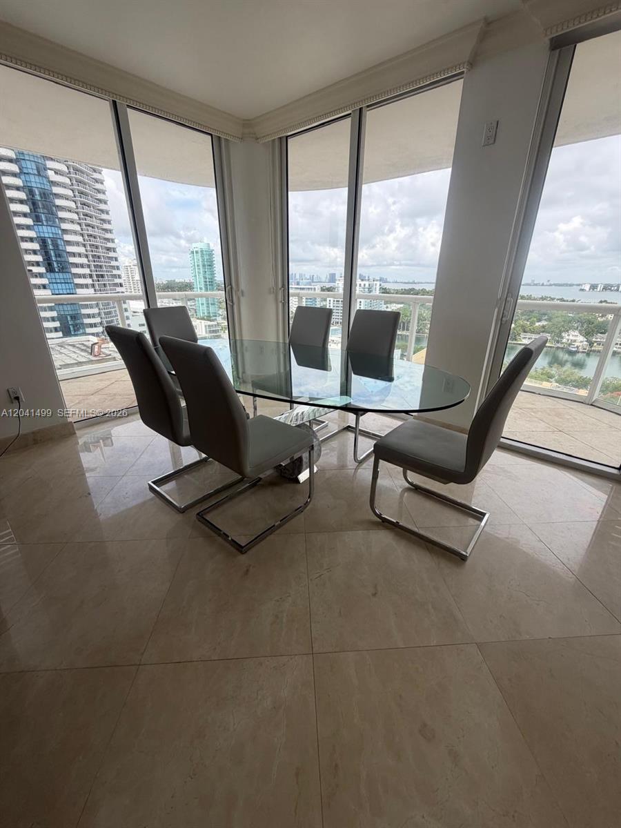 A dining area with a glass table and six chairs overlooks a city and water view — 6365 Collins Ave # 1707, Miami Beach FL 33141, MIAMI BEACH, FL
