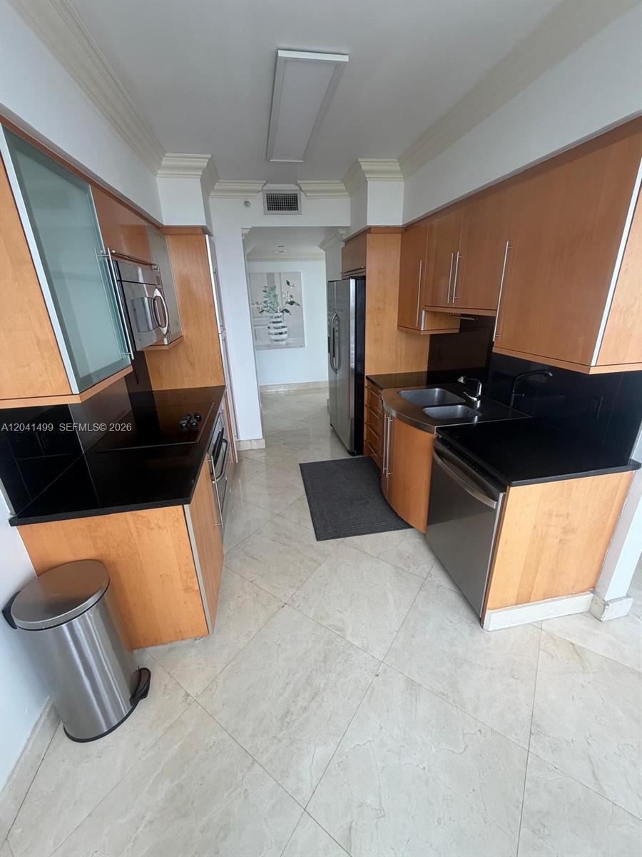 A galley kitchen features light wood cabinets, black countertops, and stainless steel appliances — 6365 Collins Ave # 1707, Miami Beach FL 33141, MIAMI BEACH, FL