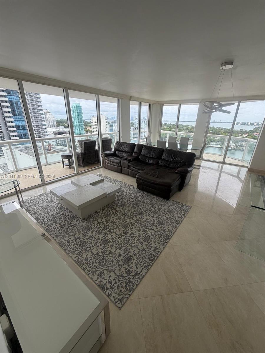 A living room features a dark leather sectional, a patterned rug, and floor-to-ceiling windows — 6365 Collins Ave # 1707, Miami Beach FL 33141, MIAMI BEACH, FL