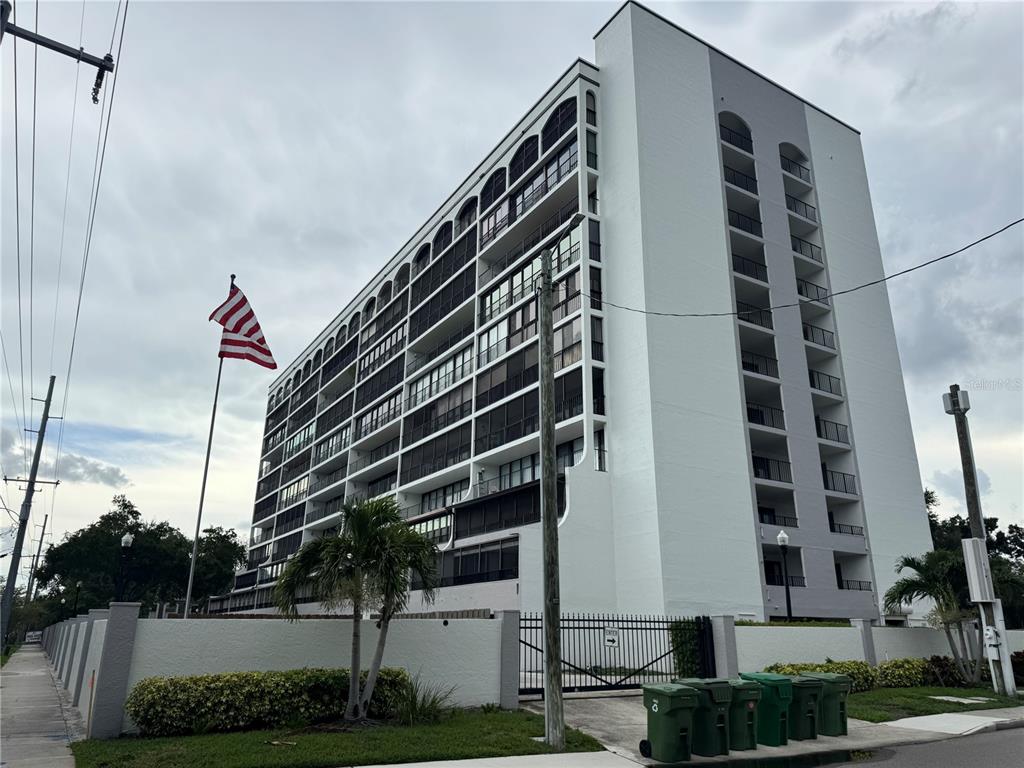 A multi-story white apartment building stands behind a fence with an American flag flying nearby — 3211 W SWANN AVENUE UNIT 1005, TAMPA, FL