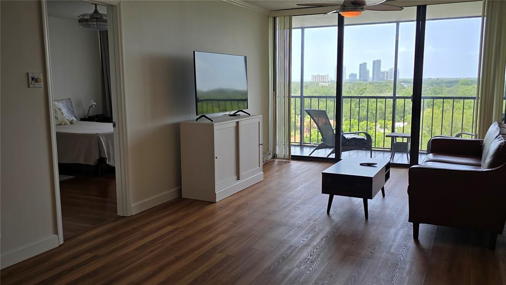 A living room features wood-look flooring, a television on a cabinet, and a balcony view — 3211 W SWANN AVENUE UNIT 1005, TAMPA, FL