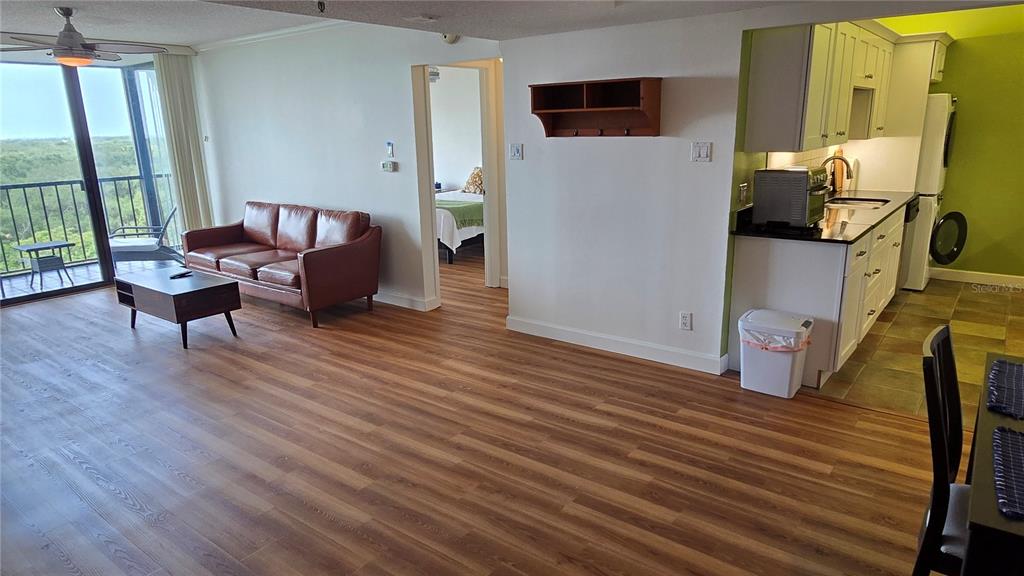 An open-concept living area features wood-look flooring, a leather sofa, and an adjacent kitchen — 3211 W SWANN AVENUE UNIT 1005, TAMPA, FL