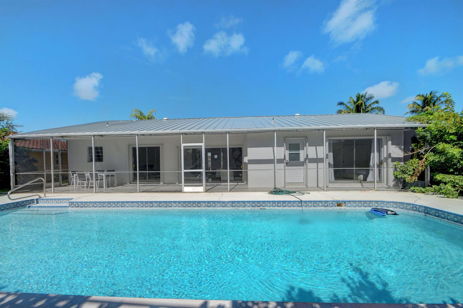 A swimming pool sits in front of a house with a screened-in patio and metal roof — 1171 Bimini Lane, Singer Island FL 33404, SINGER ISLAND, FL