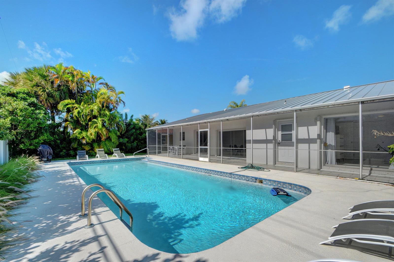 An outdoor swimming pool with a screened-in patio area and lounge chairs under a blue sky — 1171 Bimini Lane, Singer Island FL 33404, SINGER ISLAND, FL