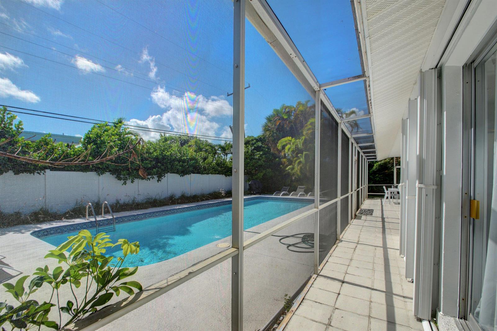 A screened-in patio overlooks a rectangular swimming pool surrounded by a white fence and trees — 1171 Bimini Lane, Singer Island FL 33404, SINGER ISLAND, FL