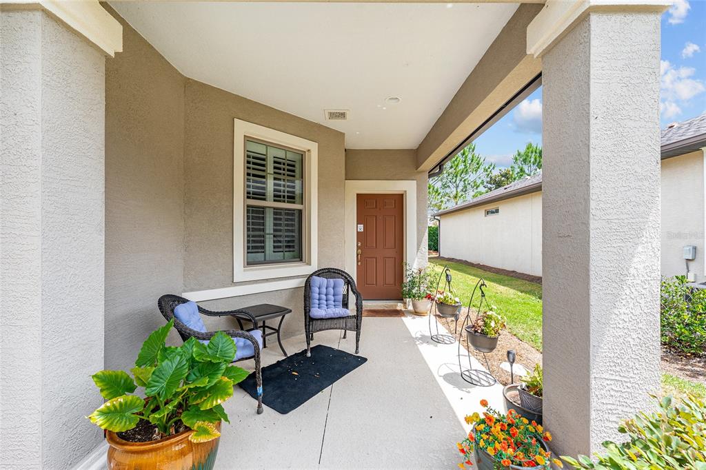 A covered front porch features a brown door, two wicker chairs, and potted plants — 9497 SW 76TH STREET, OCALA, FL