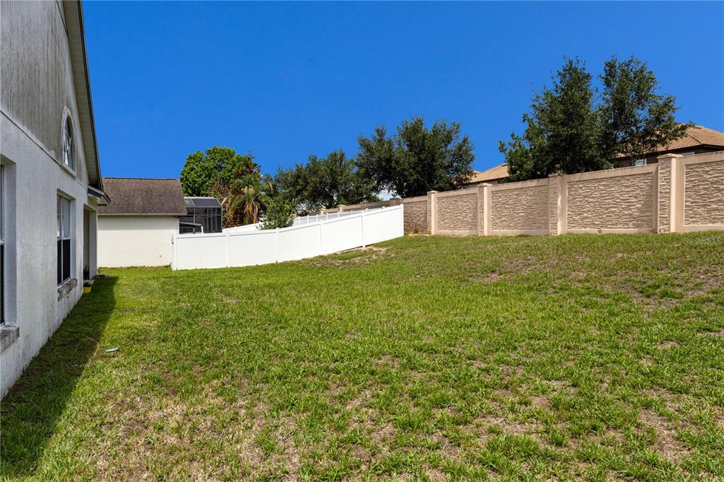 A grassy backyard features a white vinyl fence and a decorative concrete perimeter wall — 437 VIA DEL SOL DRIVE, DAVENPORT, FL