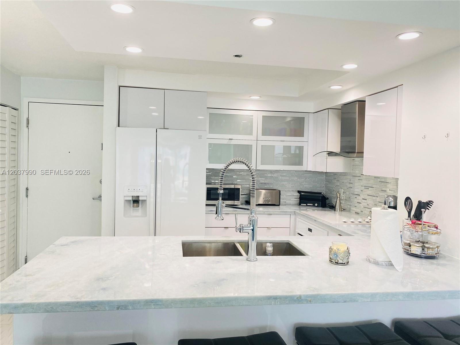 A modern kitchen features white cabinetry, a marble-topped island with a sink, and stainless appliances — 6917 Collins Ave # 1205, Miami Beach FL 33141, MIAMI BEACH, FL