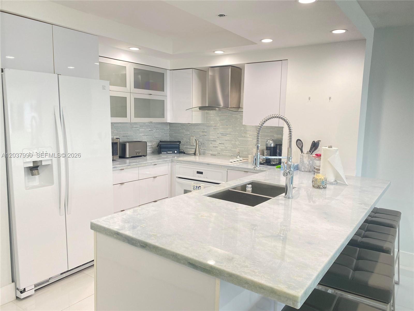 A modern kitchen features white cabinets, a large stone island with a sink, and stainless appliances — 6917 Collins Ave # 1205, Miami Beach FL 33141, MIAMI BEACH, FL