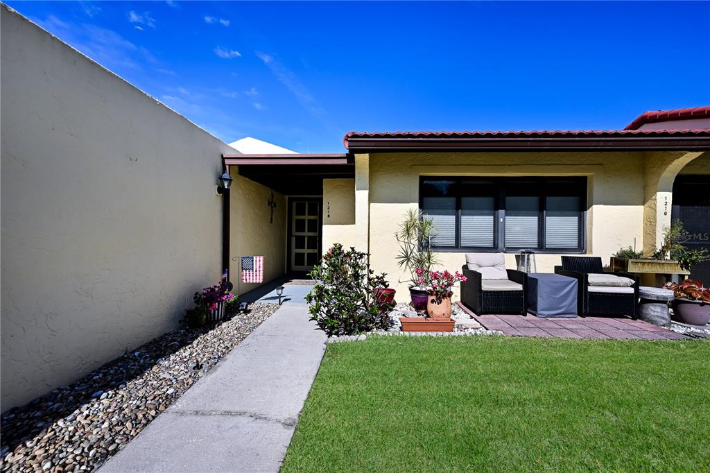 A single-story house exterior features a concrete walkway, a small patio, and a grassy lawn — 1218 56TH STREET W UNIT 1218, BRADENTON, FL