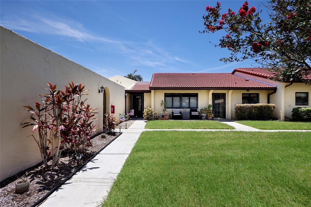 A single-story house with a red tile roof, a lawn, and a long privacy wall — 1218 56TH STREET W UNIT 1218, BRADENTON, FL