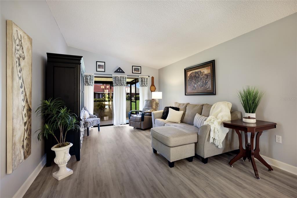 A living room features light wood-look flooring, a gray sectional sofa, and a large giraffe print — 1218 56TH STREET W UNIT 1218, BRADENTON, FL