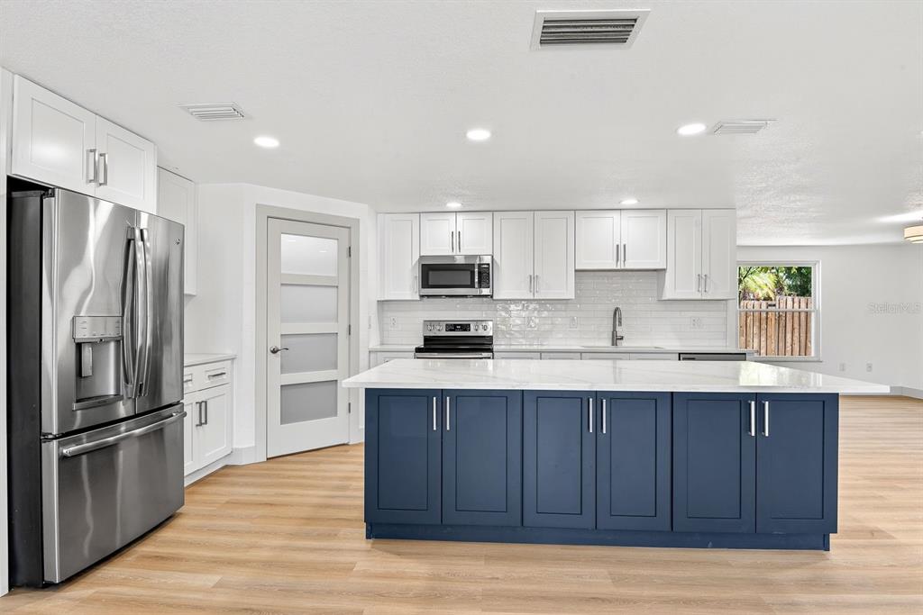 A kitchen features white upper cabinets, a blue island, stainless steel appliances, and wood flooring — 6306 37TH AVENUE W, BRADENTON, FL