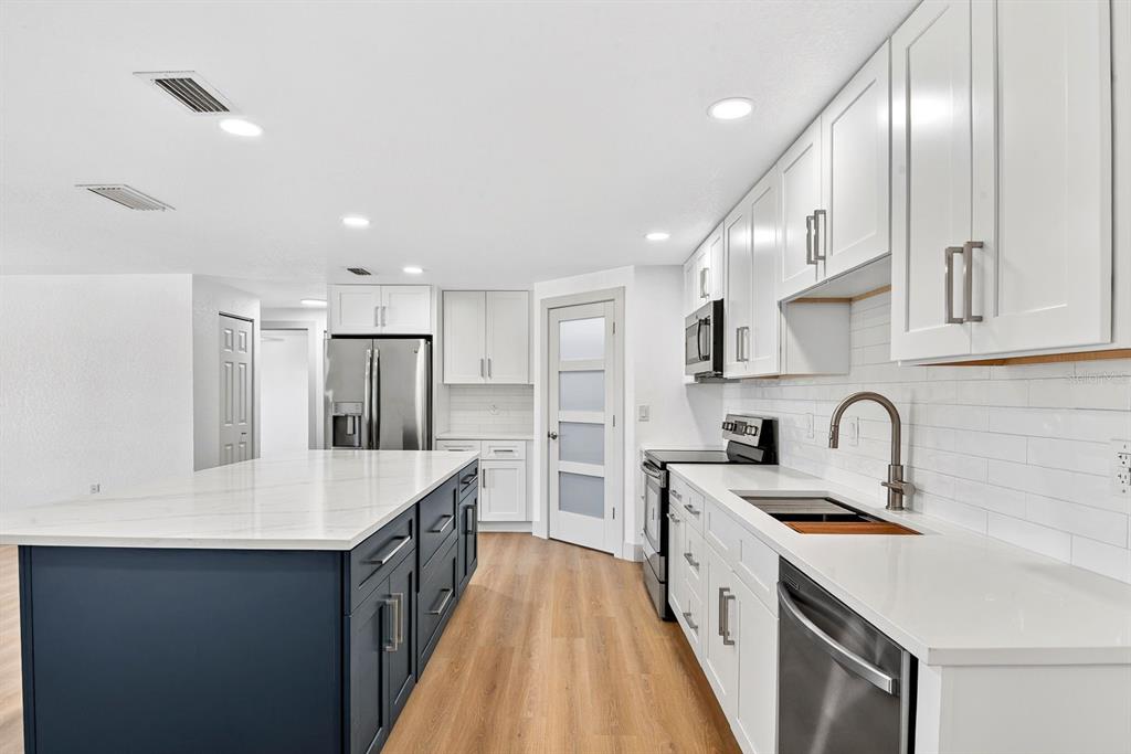 A modern kitchen features a blue island, white cabinets, stainless steel appliances, and wood flooring — 6306 37TH AVENUE W, BRADENTON, FL