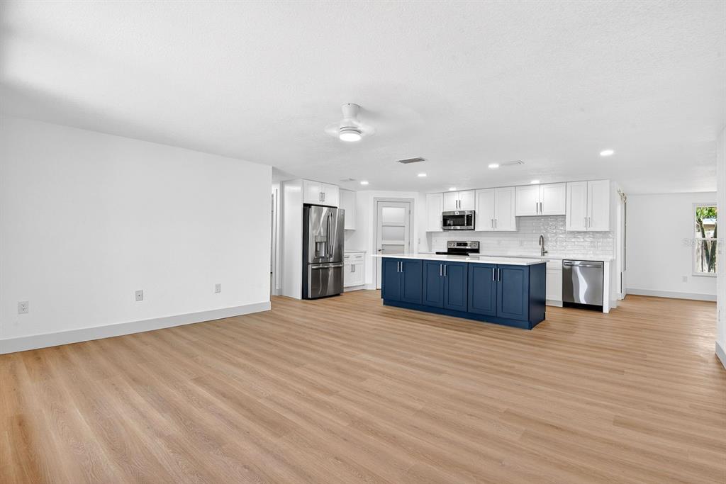 A bright, open-concept kitchen features a blue island, white cabinetry, and light wood-look flooring — 6306 37TH AVENUE W, BRADENTON, FL