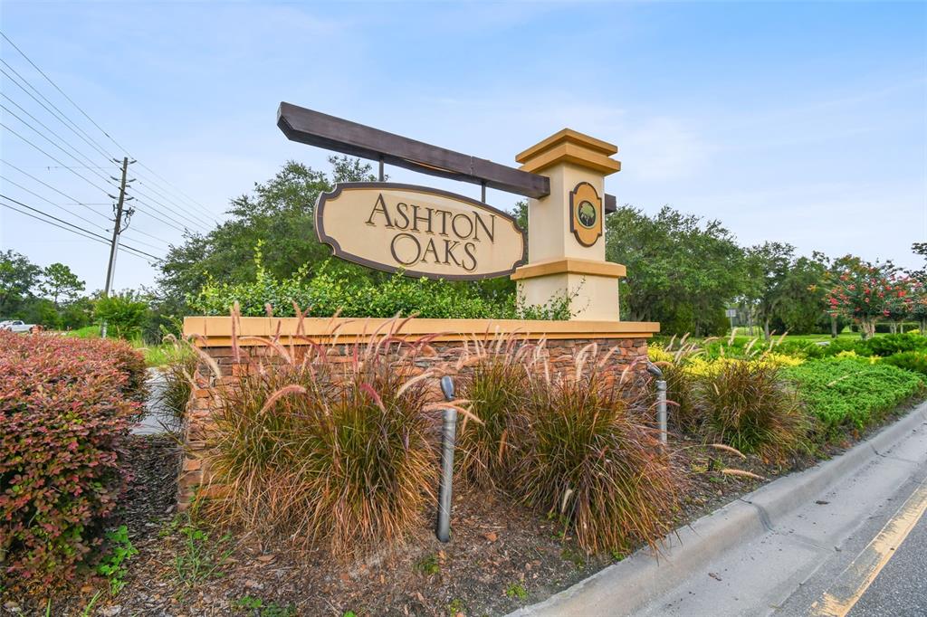 A stone and stucco monument sign for Ashton Oaks stands beside a paved road — 4329 ASHTON MEADOWS WAY, WESLEY CHAPEL, FL