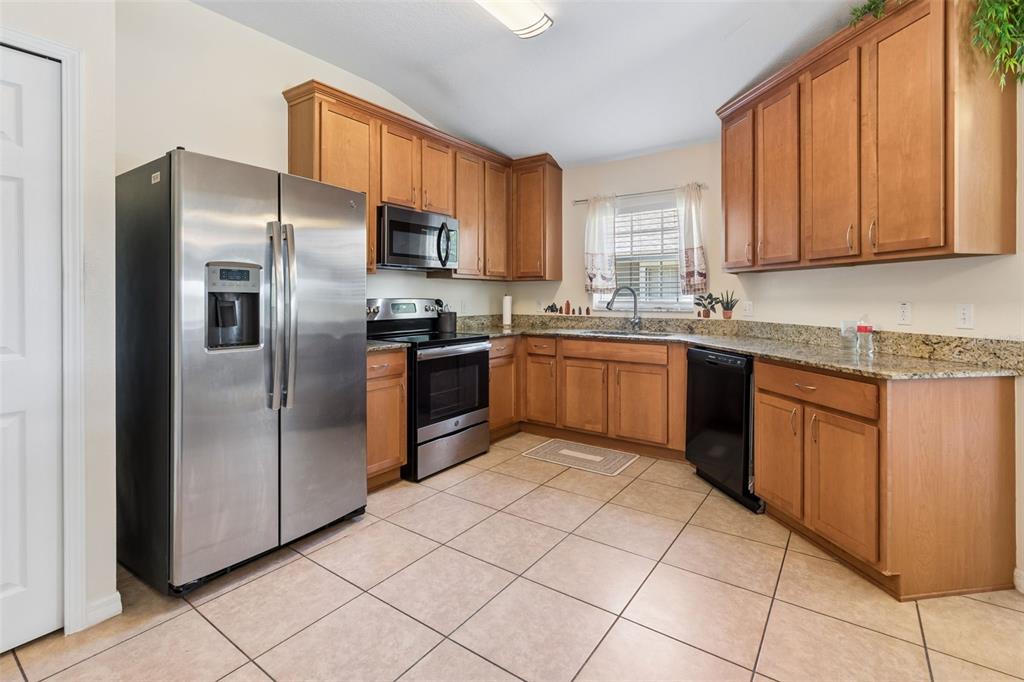 A kitchen features wood cabinets, stainless steel appliances, granite countertops, and light-colored tile flooring — 4329 ASHTON MEADOWS WAY, WESLEY CHAPEL, FL