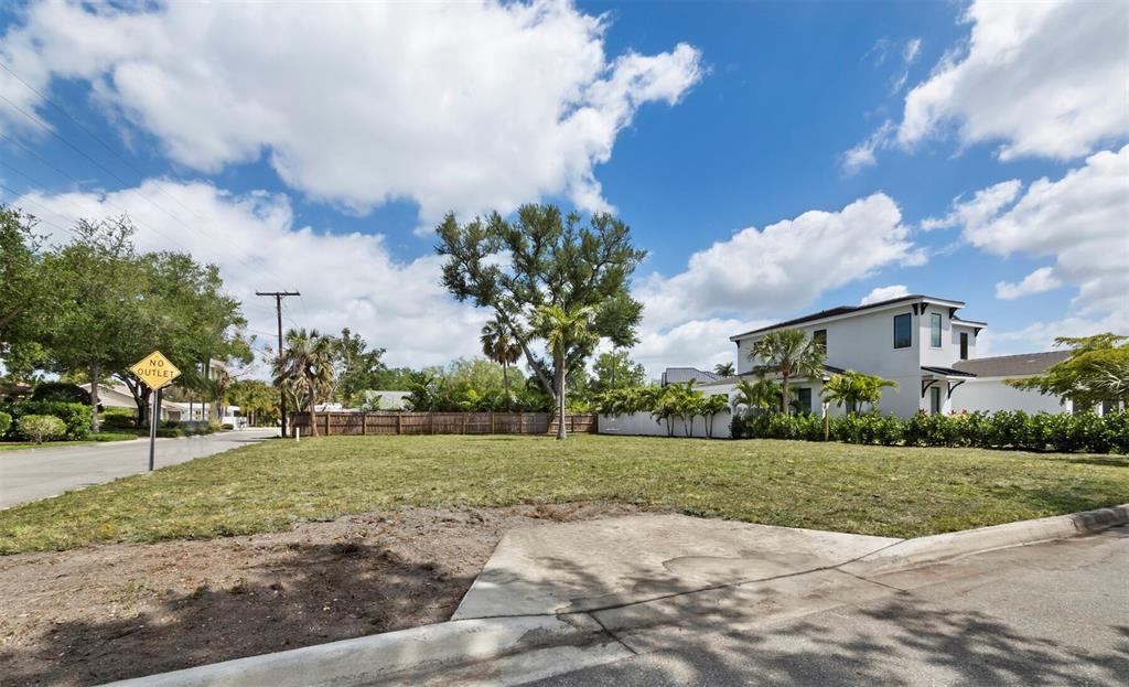 A vacant grassy lot sits between a paved street and a white two-story house — 1703 ALTA VISTA STREET, SARASOTA, FL