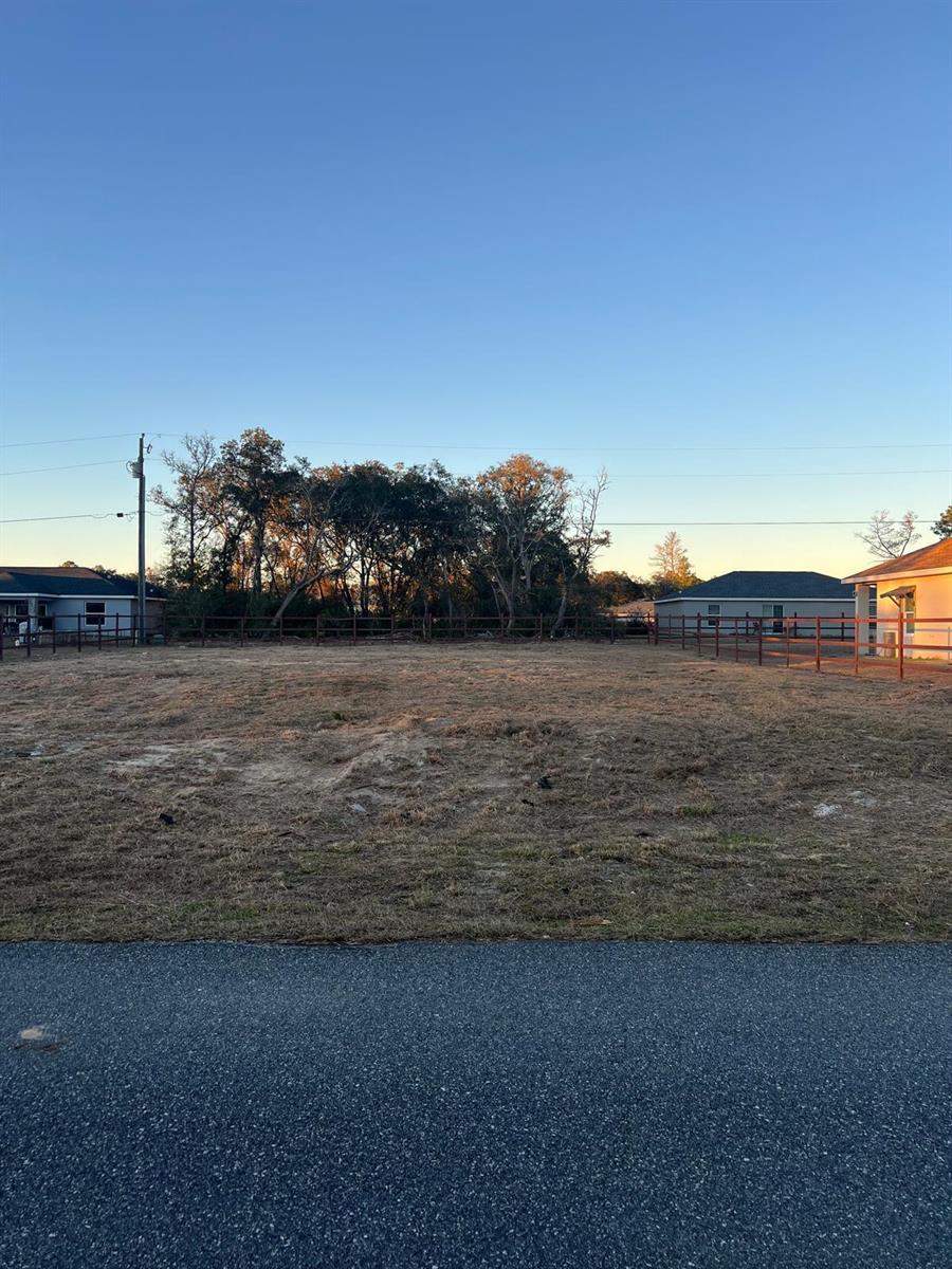 A vacant, fenced residential lot is viewed from the street under a clear blue sky — 4017 SW 133rd Loop, Ocala FL 34473, OCALA, FL