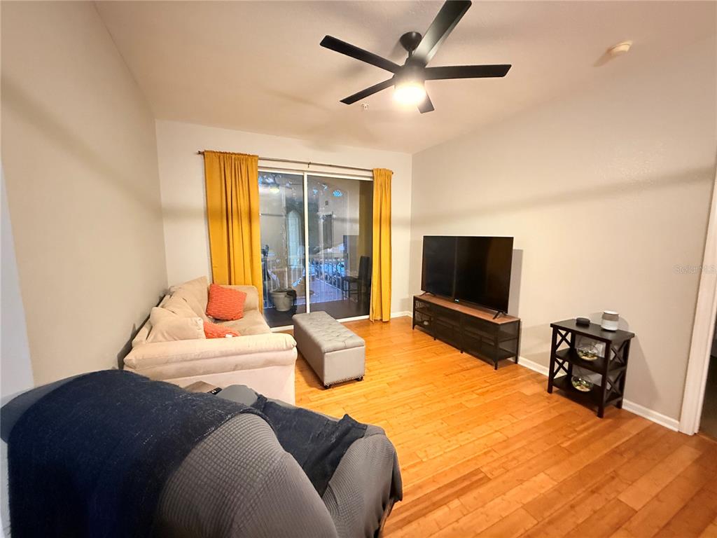 A living room features hardwood floors, a ceiling fan, a television, and sliding glass doors — 8710 SARATOGA INLET DRIVE UNIT 203, ORLANDO, FL