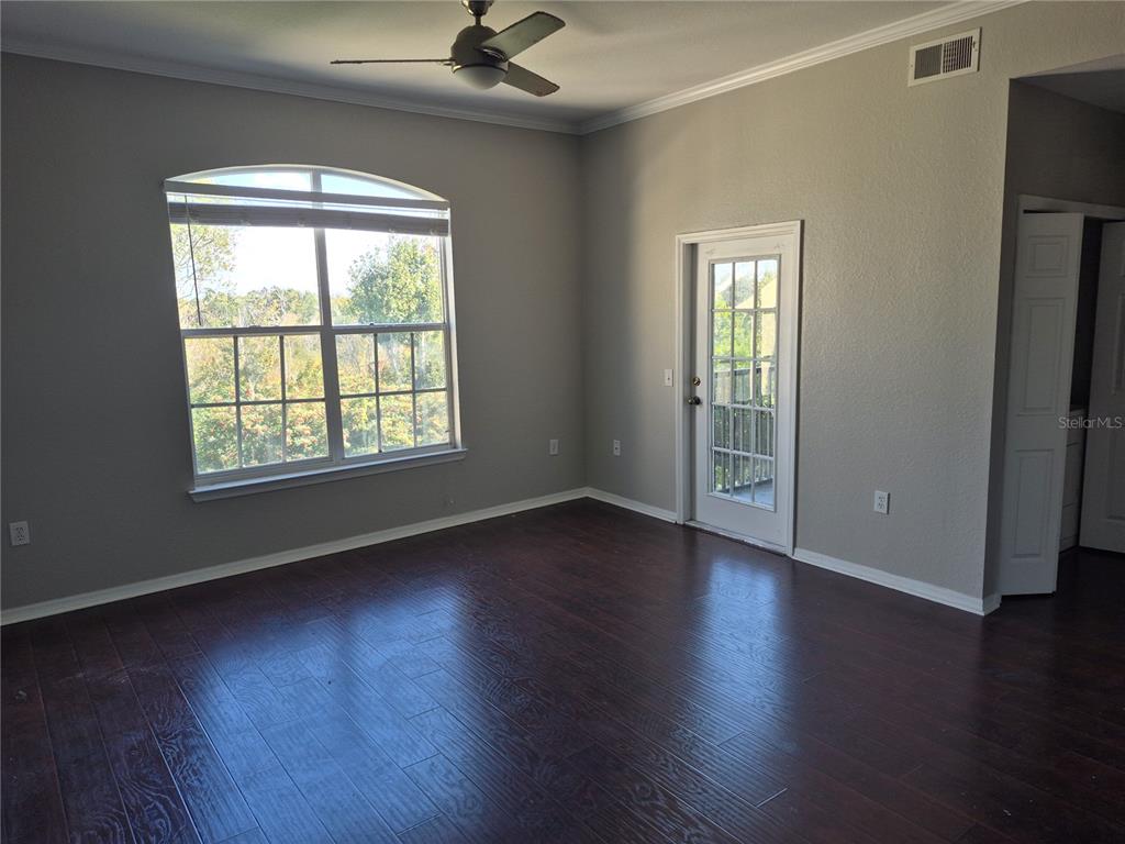 An empty room with dark wood flooring, a ceiling fan, a large window, and a door — 5146 NORTHRIDGE ROAD UNIT 309, SARASOTA, FL