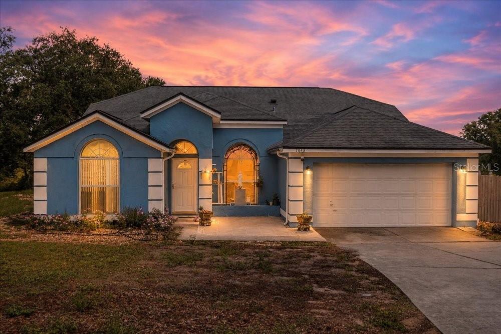 A blue single-story house with a two-car garage and arched windows at sunset — 7045 CORAL COVE DRIVE, ORLANDO, FL