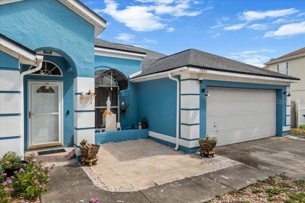 A blue house exterior features a white garage door, a front patio, and arched entryway — 7045 CORAL COVE DRIVE, ORLANDO, FL