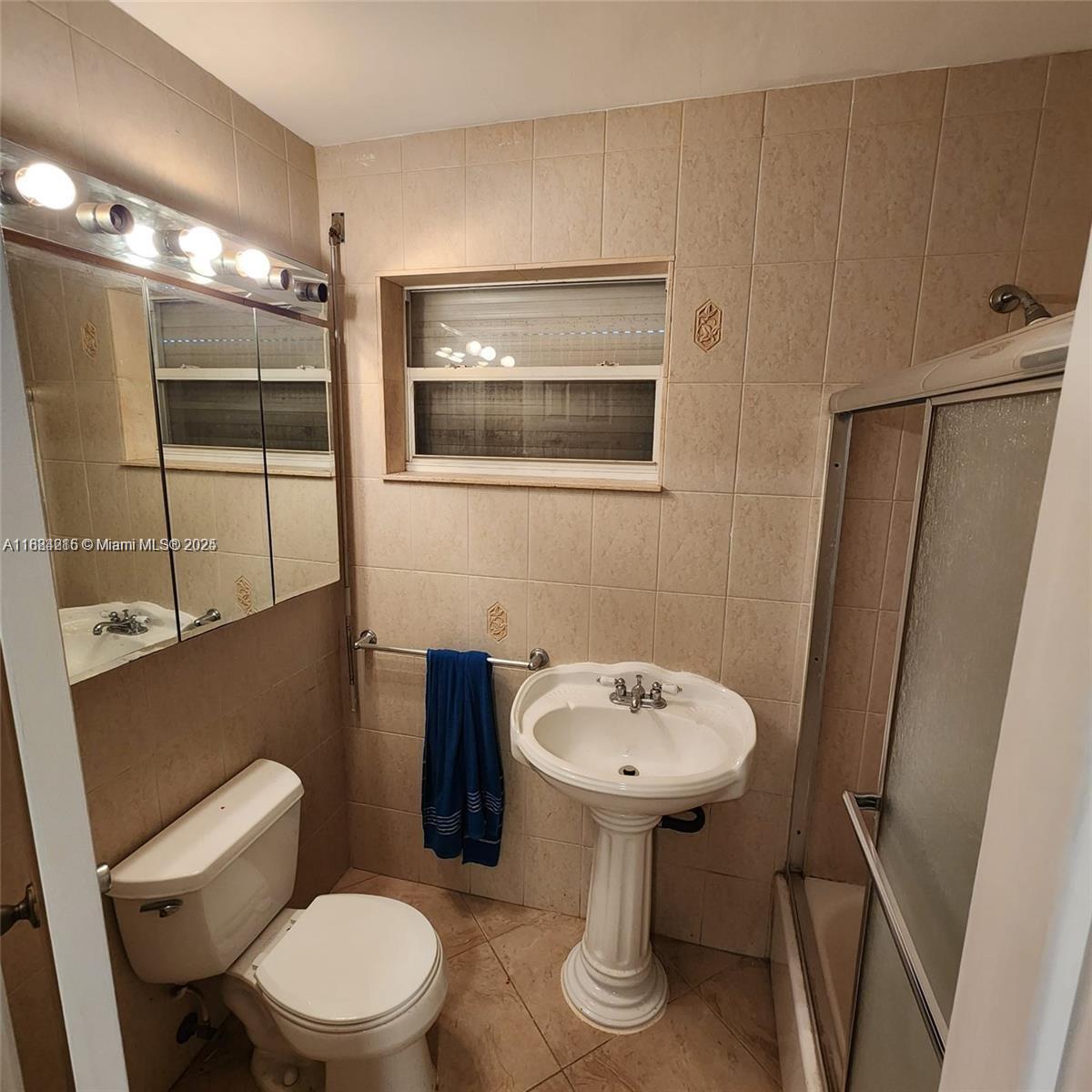 A bathroom features a pedestal sink, toilet, shower stall, and beige wall tiles — 1843 Wiley St, Hollywood FL 33020, HOLLYWOOD, FL