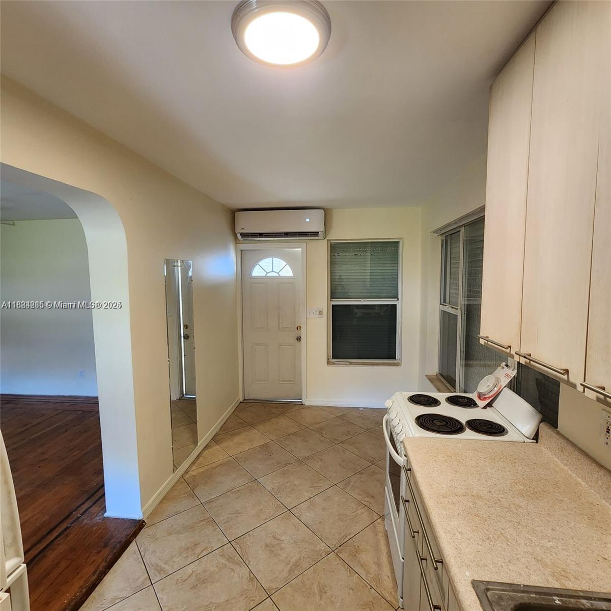 A kitchen features tile flooring, a white electric stove, and a wall-mounted air conditioning unit — 1843 Wiley St, Hollywood FL 33020, HOLLYWOOD, FL