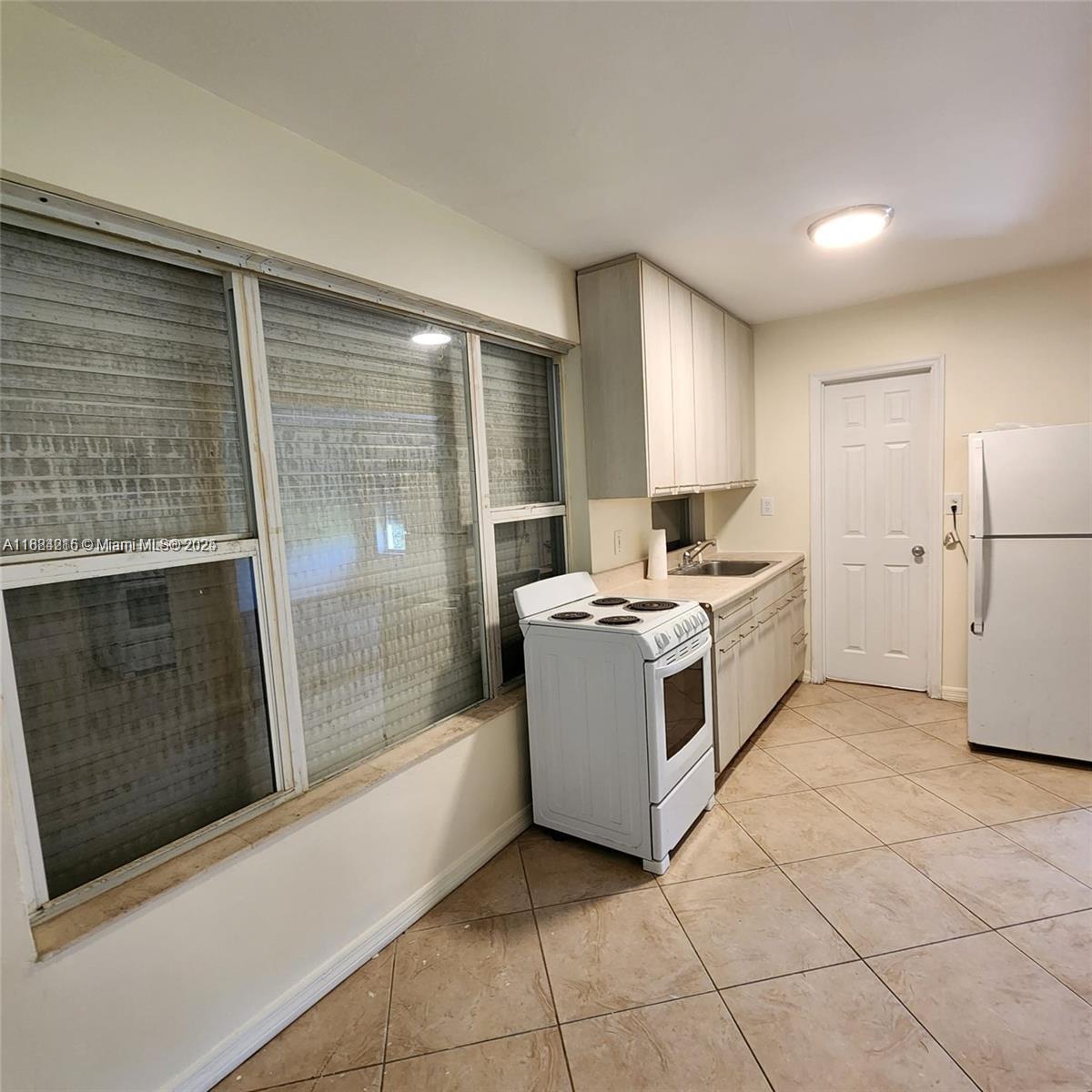 A kitchen features white appliances, light-colored cabinetry, a window with shutters, and tiled flooring — 1843 Wiley St, Hollywood FL 33020, HOLLYWOOD, FL