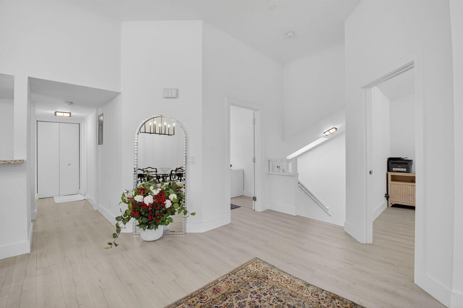 A bright, white-walled hallway features light wood flooring, an arched mirror, and a staircase — 5328 Buckhead Circle # 2020, Boca Raton FL 33486, BOCA RATON, FL