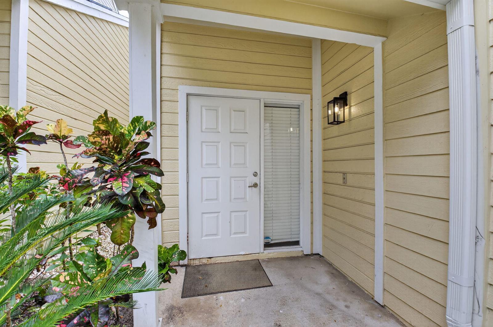 A white front door with a side window sits under a covered porch with yellow siding — 5328 Buckhead Circle # 2020, Boca Raton FL 33486, BOCA RATON, FL