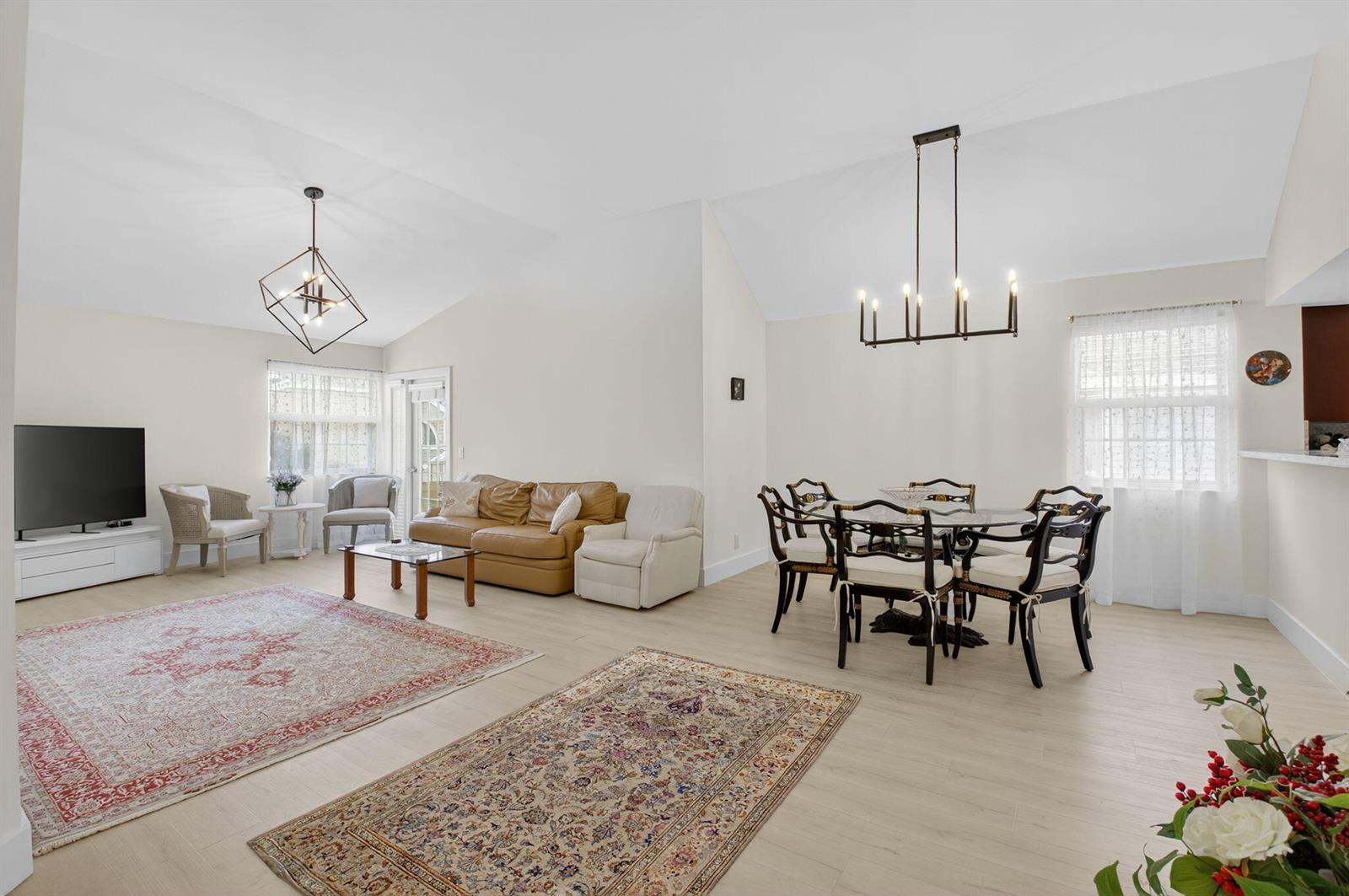 An open-concept living and dining area features vaulted ceilings, light wood flooring, and two rugs — 5328 Buckhead Circle # 2020, Boca Raton FL 33486, BOCA RATON, FL