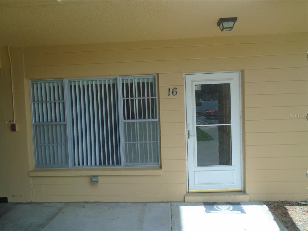 The exterior of a residential unit features a white door, a large window, and number 16 — 2466 ECUADORIAN WAY UNIT 16, CLEARWATER, FL