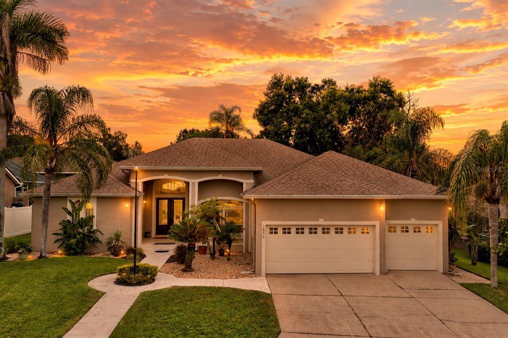 A single-story house with a three-car garage and palm trees under a vibrant sunset sky — 2856 MERIDIAN POINT LANE, LAKELAND, FL