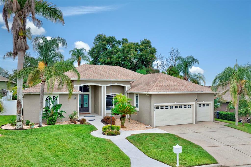 A single-story suburban house with a tan stucco exterior, a three-car garage, and palm trees — 2856 MERIDIAN POINT LANE, LAKELAND, FL