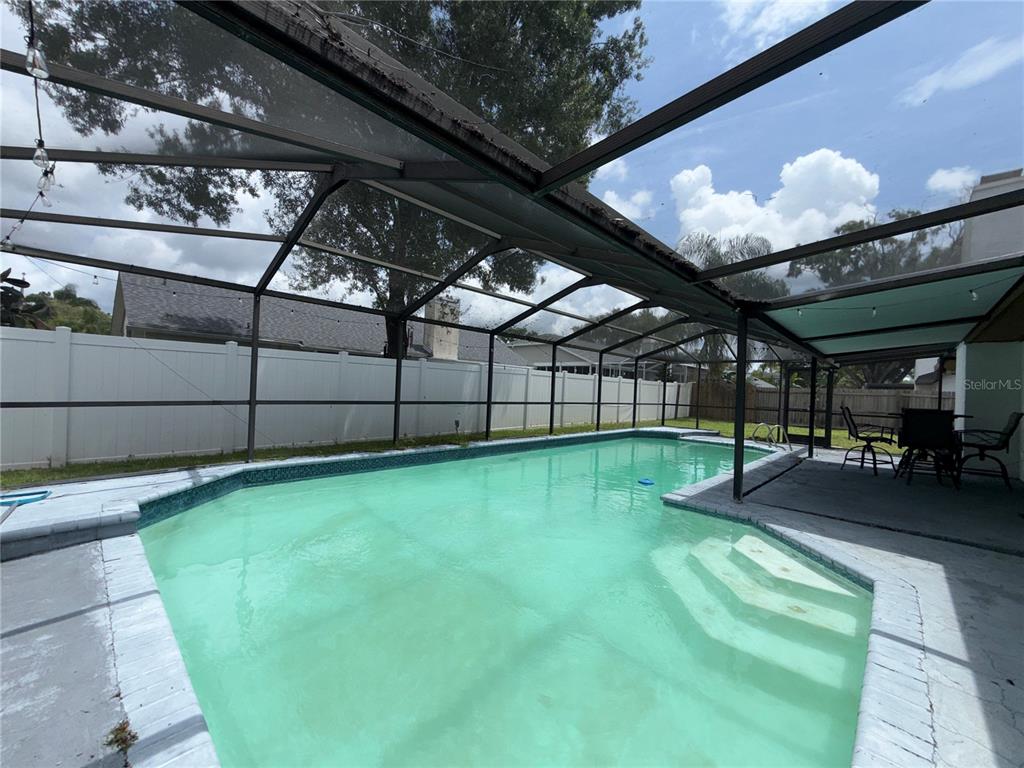 A screened-in swimming pool with a concrete deck and a white vinyl privacy fence — 4715 KEMBLE COURT, TAMPA, FL