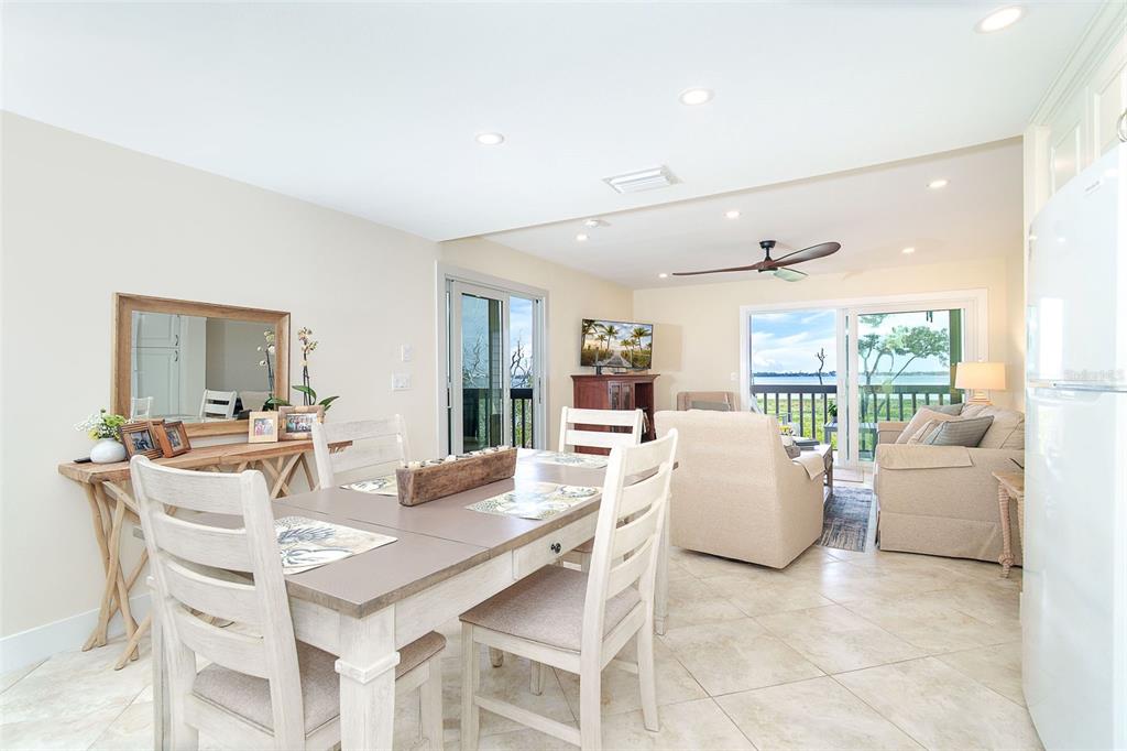 A dining area with a wooden table and chairs opens into a living room with water views — 9200 LITTLE GASPARILLA ISLAND UNIT 403, PLACIDA, FL