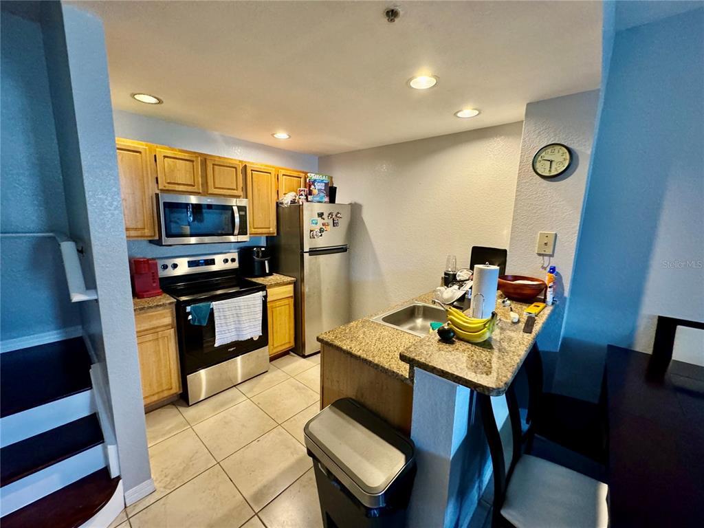 A kitchen features light wood cabinets, stainless steel appliances, granite countertops, and tile flooring — 4000 SAN GALLO DRIVE UNIT 105, KISSIMMEE, FL