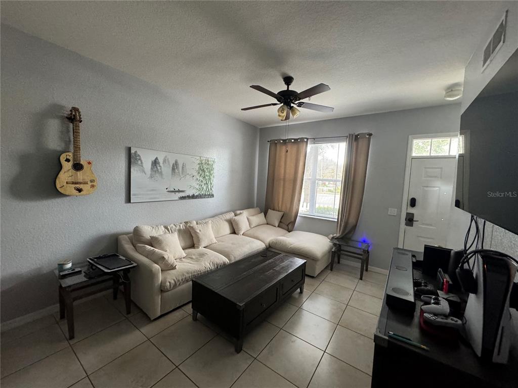 A living room features a beige sectional sofa, a dark coffee table, and a wall-mounted guitar — 4000 SAN GALLO DRIVE UNIT 105, KISSIMMEE, FL