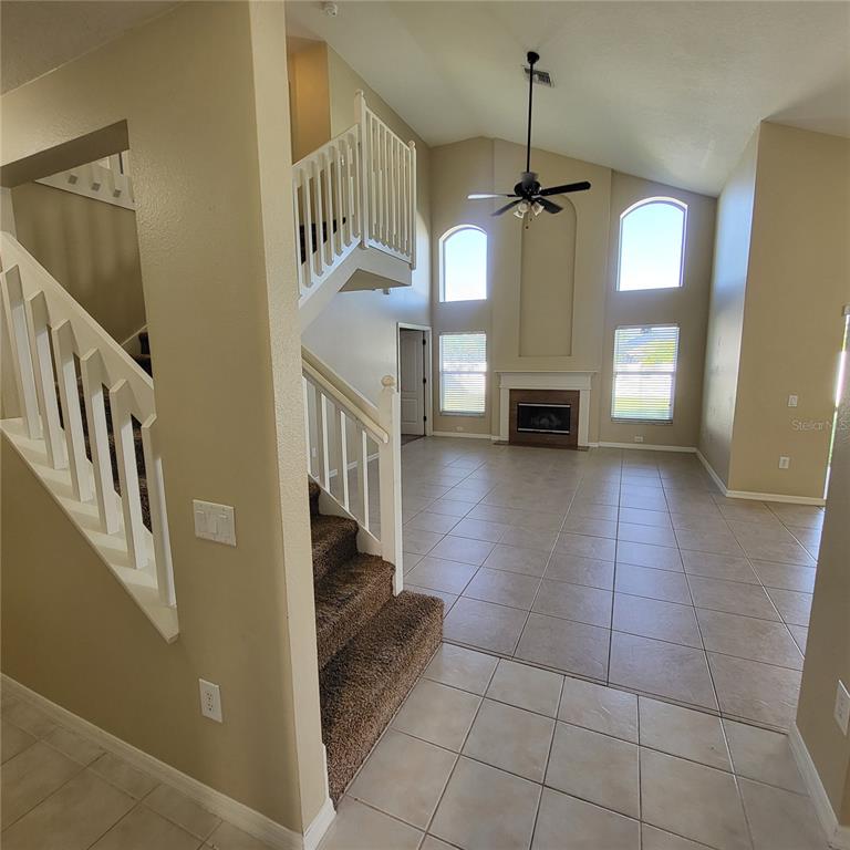 A living room with a fireplace, vaulted ceiling, tile floors, and a carpeted staircase — 25903 BLOOMSBURY COURT, LAND O LAKES, FL