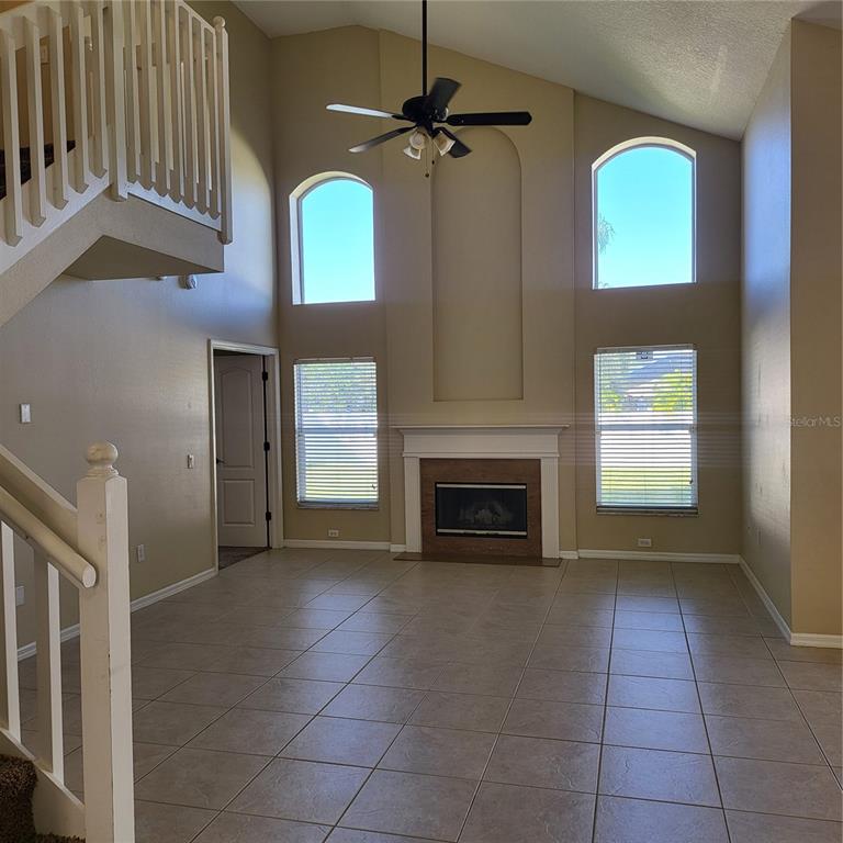 A living room with a fireplace, vaulted ceilings, tiled floors, and a staircase — 25903 BLOOMSBURY COURT, LAND O LAKES, FL