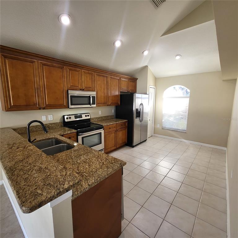A kitchen features wood cabinets, granite countertops, stainless steel appliances, and light-colored tile flooring — 25903 BLOOMSBURY COURT, LAND O LAKES, FL